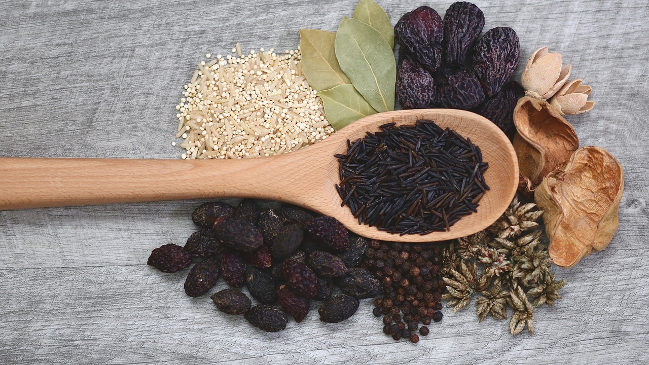 Varietet af krydderier og korn på træske og træbord, inklusive sort ris, havsalt, tørrede frugter og laurbærblade.