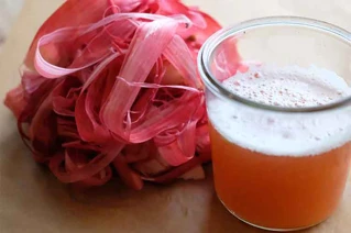 Et glas med lyserød kombucha ved siden af en bunke fermenterede rødbeder på et træbord.