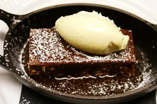 Lækker brun brownie med stødt sukker og en klat vaniljeis på en sort stegepande, servering på restaurant