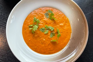 Hjemmelavet tomatsuppe med friske krydderurter i en hvid skål på et mørkt bord.