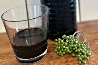 Enkely glas med mørk saft og en klase hyldebær ved siden af