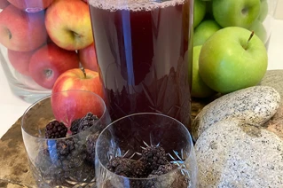 Tre glas med rød saft og æbler i baggrunden