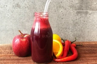 Flaske med rød juice, friske røde æbler, appelsinskiver og chili på træbord.