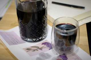 En karaffel og et glas med rødvin på et bord med en åben bog, en kuglepen og brevpapir med blomstermotiv.