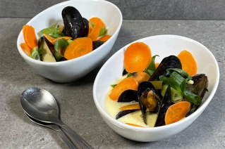 Skåle med en cremet suppe med muslinger, gulerøder og forårsløg