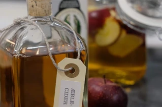 Flaske med æblecider og friske æbler på køkkenbord, husholdningsprodukter, hjemmebrygning.