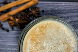 Nærbillede af glas med chai latte med kanelstænger ved siden af