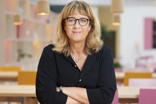 CEO af Coor, AnnaCarin Grandin, med briller smiler forsigtigt i et moderne kontorområde.