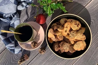 Hyggeligt eftermiddagskaffe med småkager og juledekoration på træbord.