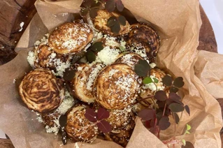 Friske danske æbleskiver med flormelis og røde skovsyreblade serveret i brunt bagepapir.