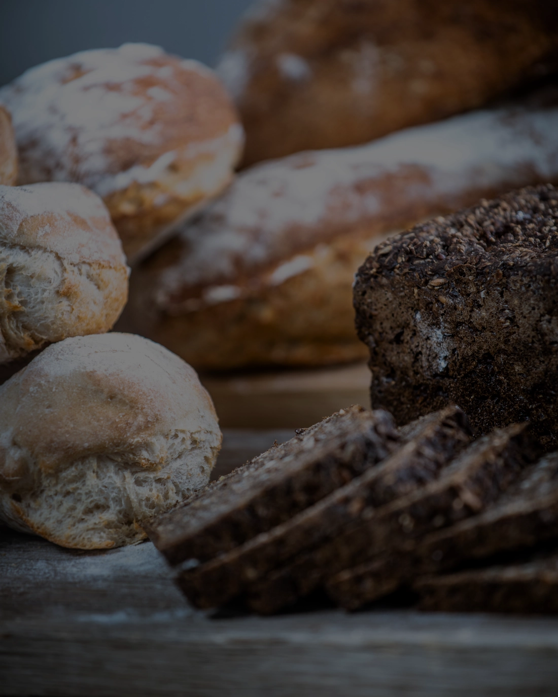 Diverse udvalg af friskbagt brød på træbaggrund, inklusive boller og rugbrød.