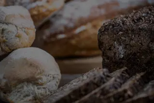 Diverse udvalg af friskbagt brød på træbaggrund, inklusive boller og rugbrød.