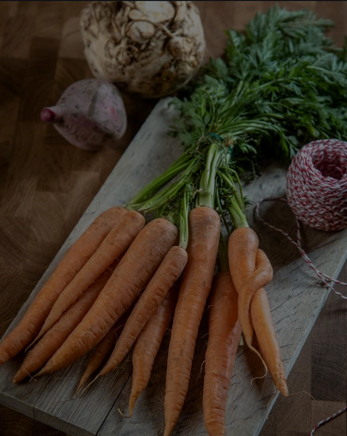Frisk økologiske gulerødder på træskærebræt med knoldselleri og rødbede i baggrunden - sund madlavning ingredienser.