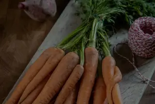 Frisk økologiske gulerødder på træskærebræt med knoldselleri og rødbede i baggrunden - sund madlavning ingredienser.