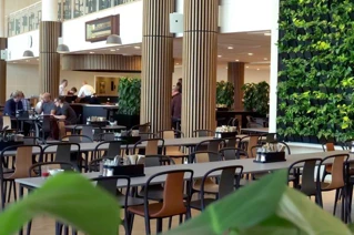 Moderne kantine med planter og spisende personer i et lyse lokaler.