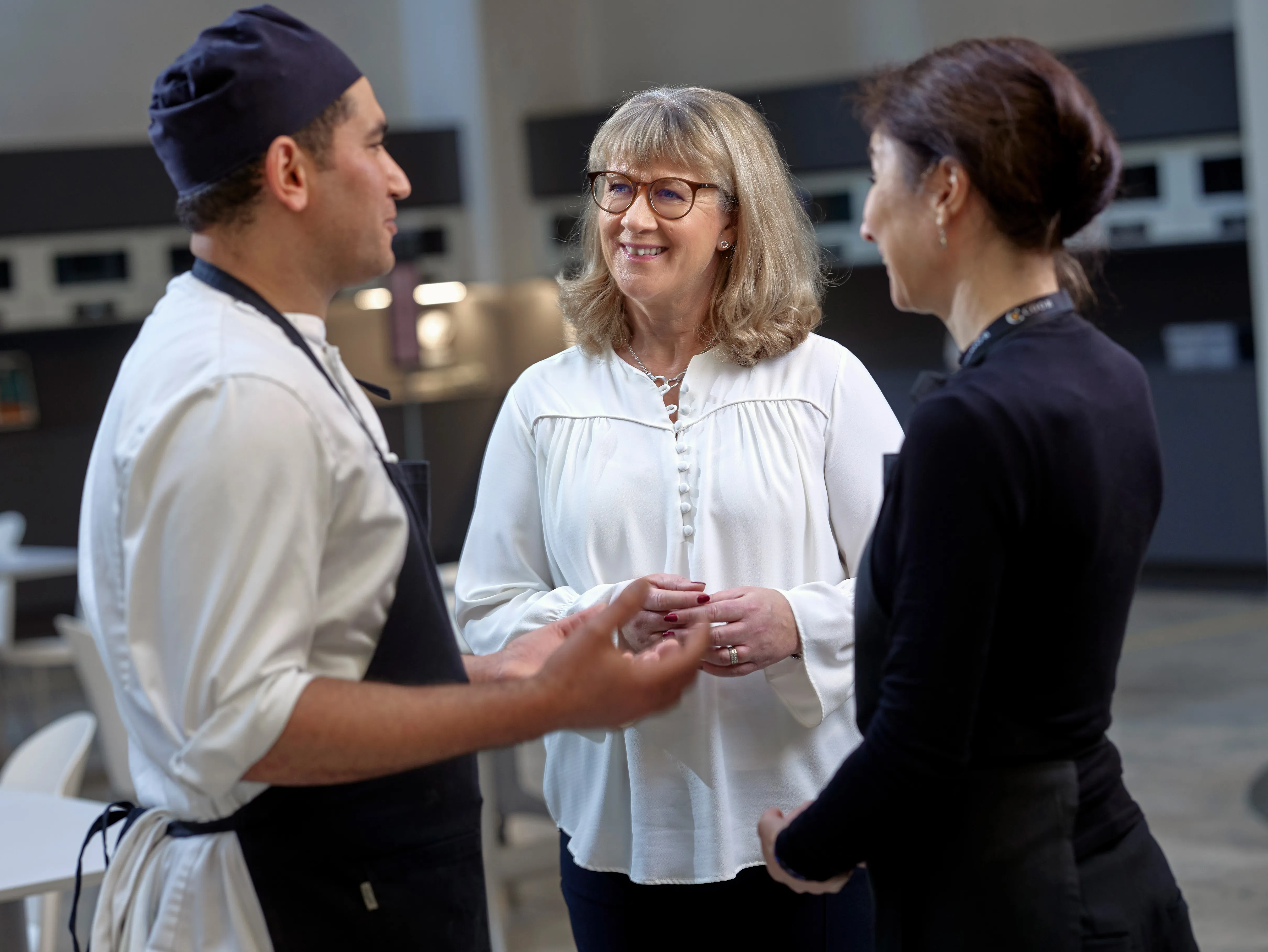 Kok i samtale med to kvinder i et professionelt køkkenmiljø.