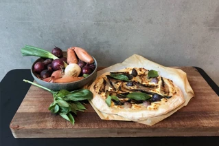 Træskærebræt med én pizza og skål med grøntsager