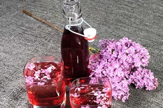 Glas flaske med rød saft og blomster buketter ved siden af