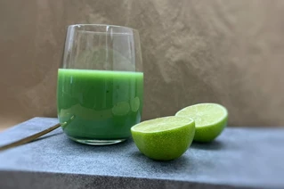 Glas med grønt juice og en skåret lime ved siden af