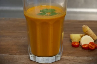 Et enkelt glas med orange suppe og pynt på toppen