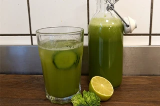 Et glas med grøn juice og en flaske der indeholder det samme til ventre for
