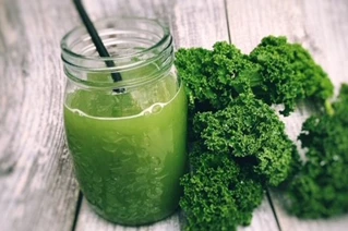 Grøn juice med sugerør og buske af grønkål ved siden af