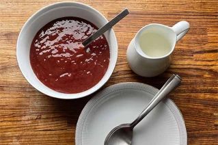 Hvid skål med rød rabarbergrød og en ske