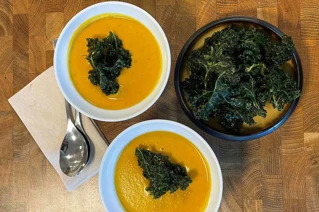 Hvide skåle med gulerodssuppe og grønkål