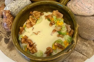 Kartoffelsuppe i skål med svampe og grøntsager, omringet af stenbrød på træunderlag.